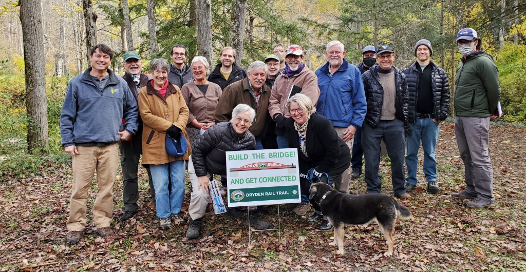 Group of people cluster around "Build the Bridge" sign on Dryden Rail Trail.